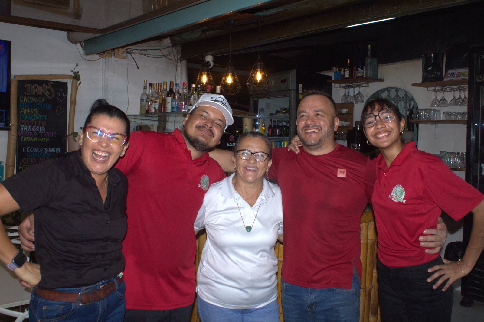 El equipo de Mambo Italiano sonriendo detrás de la barra, con la camiseta roja del logo