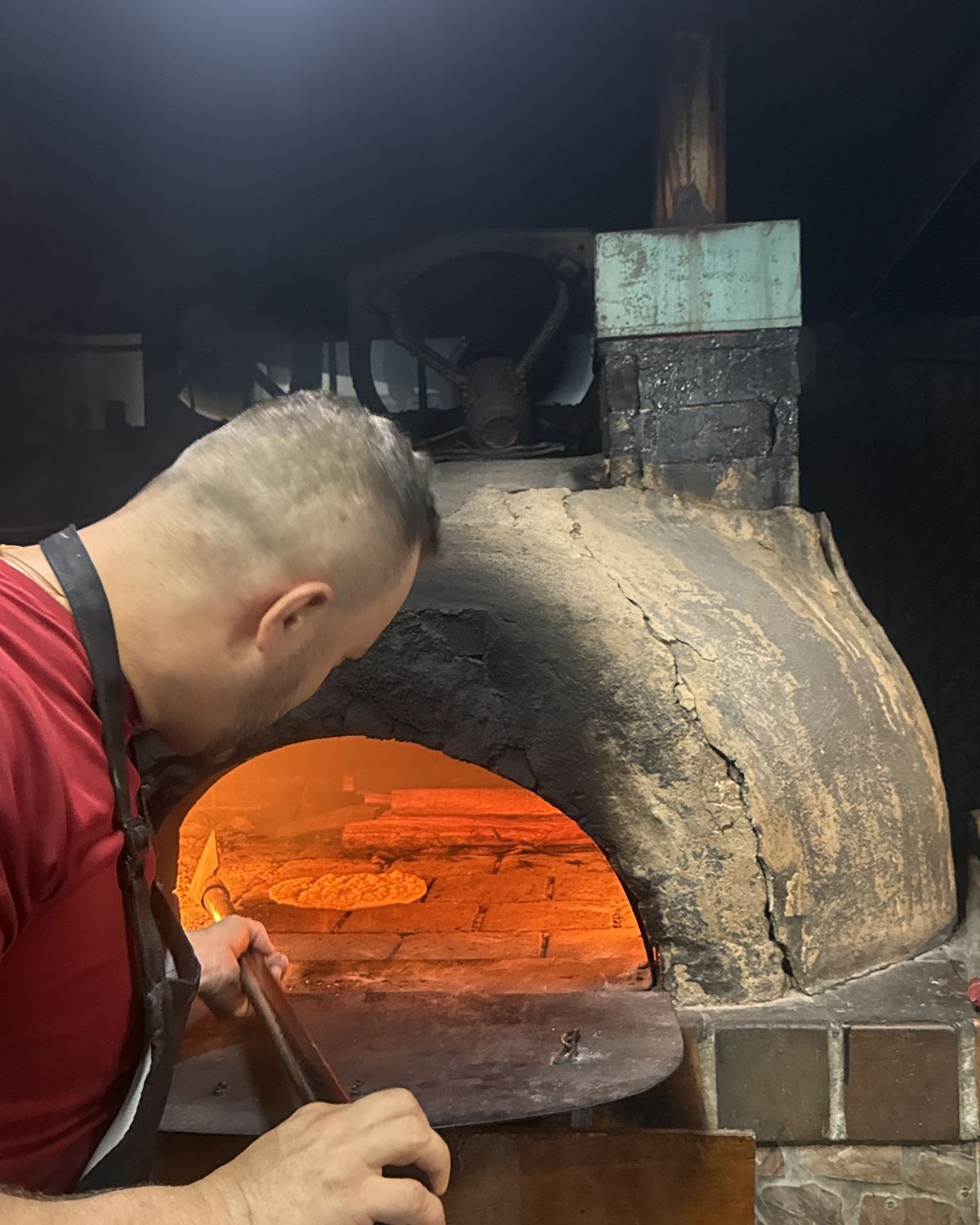 El pizzaiolo de Mambo Italiano metiendo una pizza con la pala en el horno de leña encendido